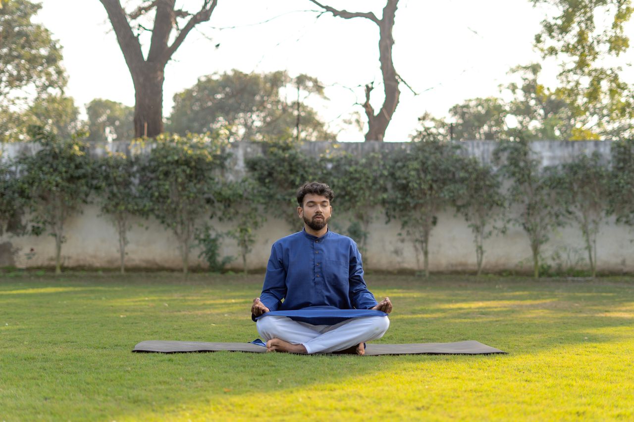 services-02 South Asian man meditating outdoors in a blue kurta, practicing yoga for wellness.
