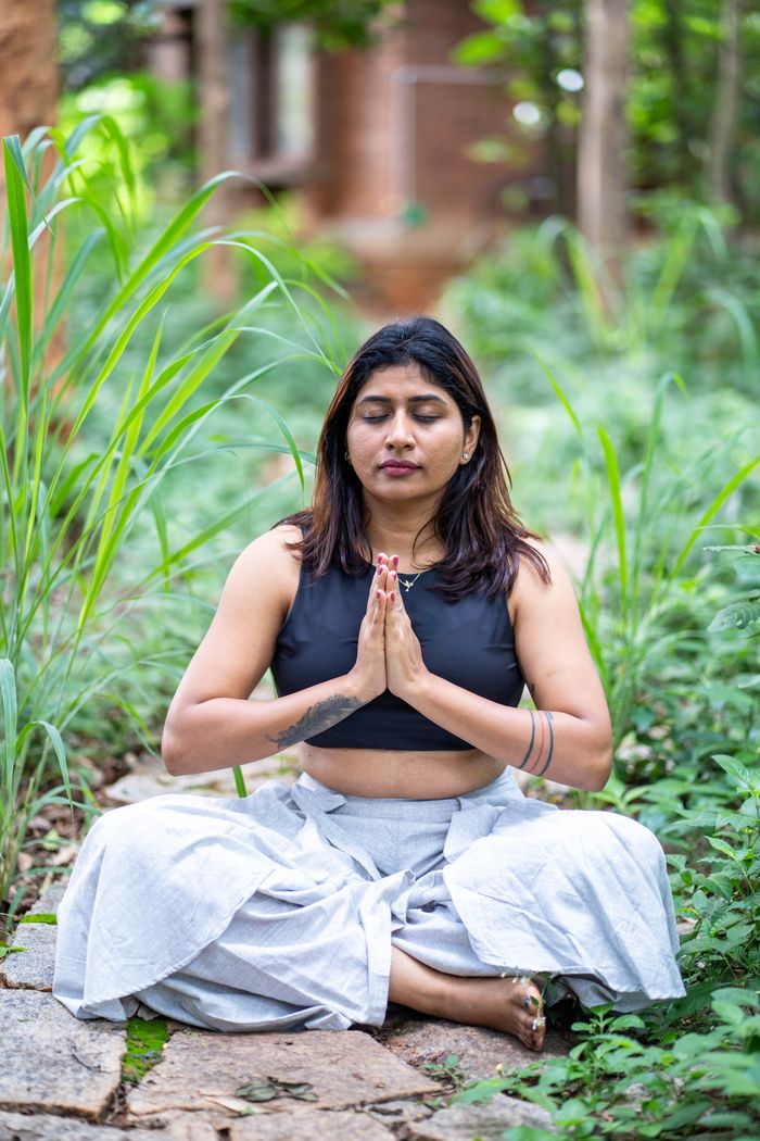 Woman meditating outdoors surrounded by lush greenery, embodying peace and mindfulness.