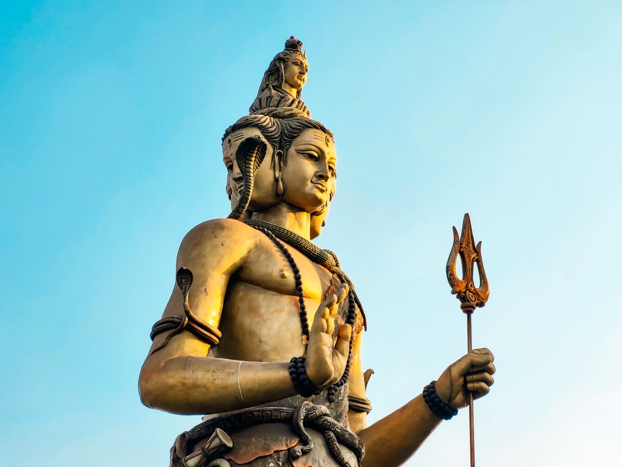 about-us-01 A stunning statue of Shiva with blue sky backdrop, showcasing intricate detail and cultural significance.