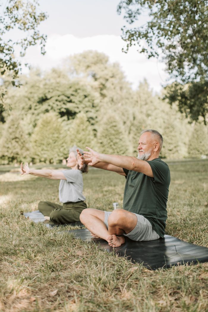 services-03 Elderly couple performing yoga stretches on mats in a serene park setting.
